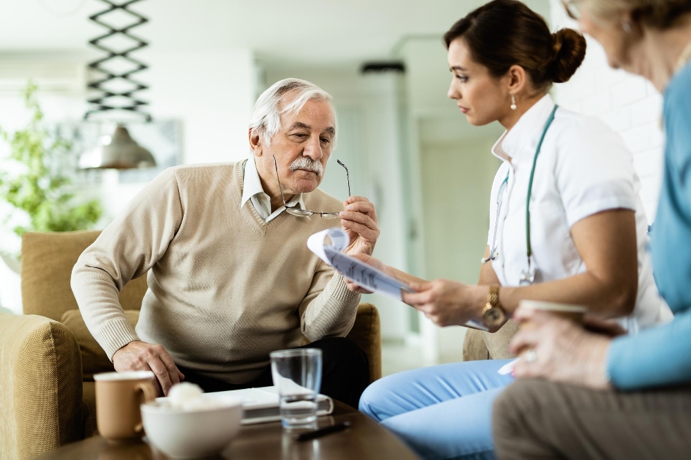 A senior man and a healthcare worker reviewing medical reports during a home visit.